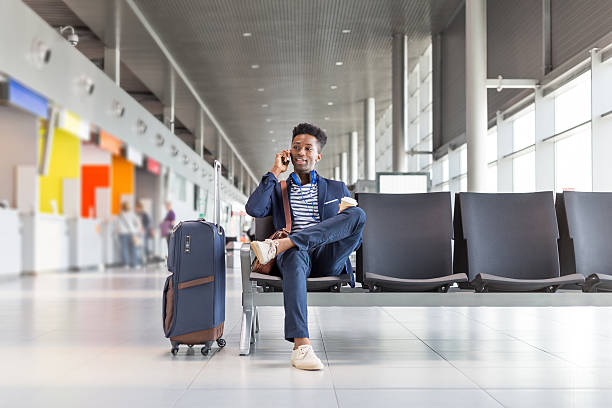 istockphoto-621595930-612×612 Young african businessman waiting for flight at the airport lounge and talking on mobile phone. Businessman in casuals sitting on chair and waiting for plane.